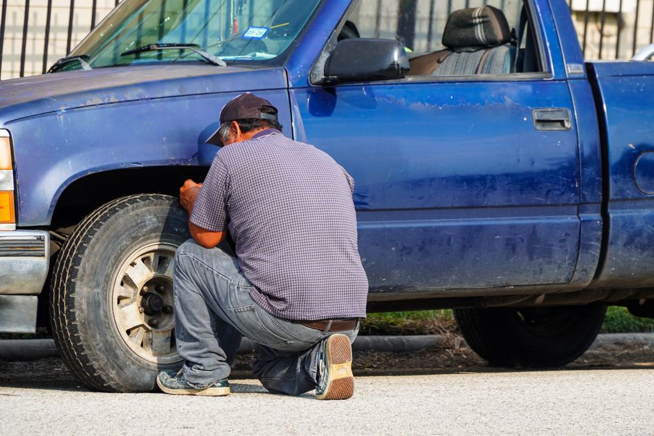 A man attentively repairing a flat tire on a blue truck in sunny Houston, Texas.