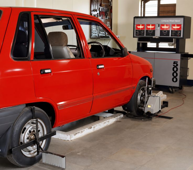 Red compact car in an automotive workshop undergoing computerized wheel alignment service.